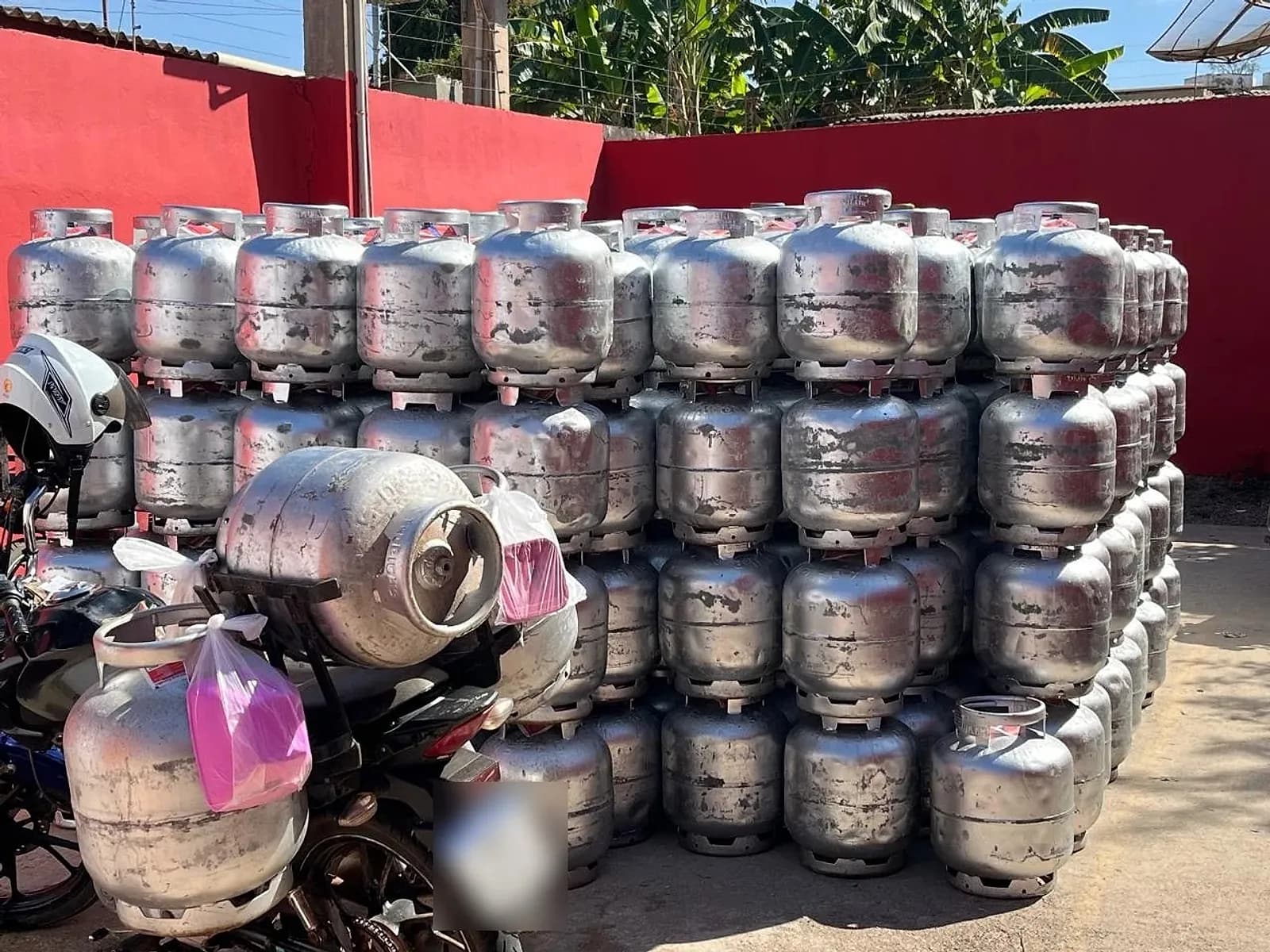 Pátio da Sad Dias Gás com centenas de botijões empilhados junto ao muro vermelho e uma moto de entrega carregada